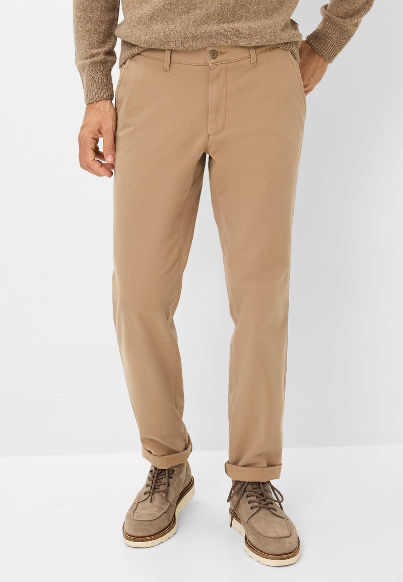 Beige katoenen broek met een slim fit, met een knoopsluiting, opgerolde manchetten en zijzakken, gecombineerd met bruin suède laarzen.