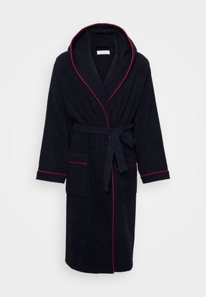 Accappatoio blu scuro con cappuccio, bordature rosse lungo i margini, cintura da annodare e due tasche frontali. Realizzato in morbido tessuto testurizzato.