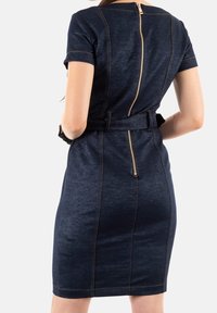 Navy sininen farkkuhamonen, jossa on lyhyet hihat, sovitettu muoto, näkyvät saumat ja takana vetoketju. Mukana on kangashihna vyötäröllä.