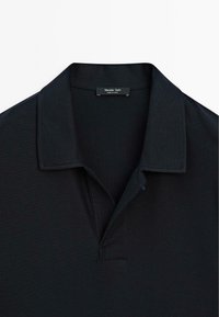 Polo nero con tessuto testurizzato, colletto a scollo e patta con due bottoni. L'etichetta riporta "Massimo Dutti, Made in China."
