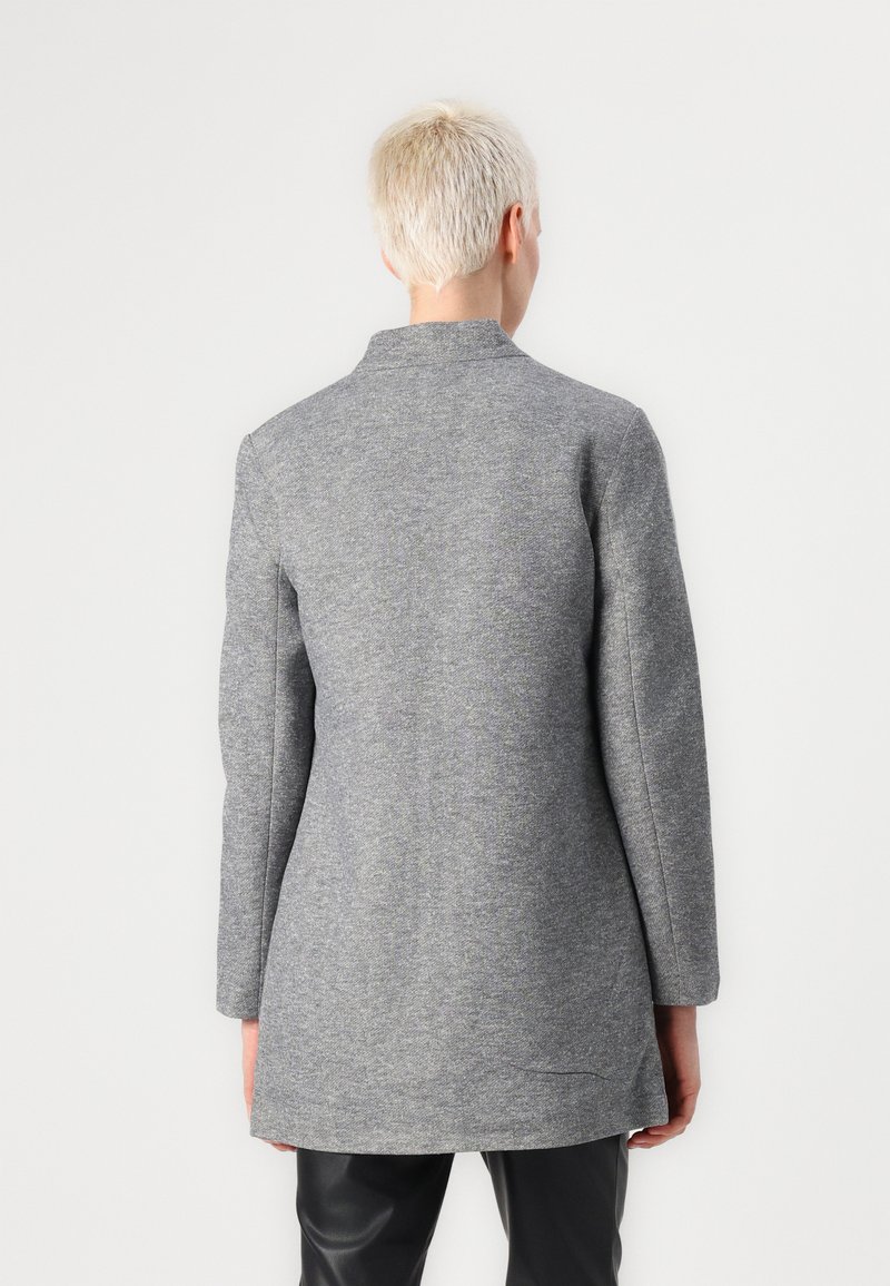 Grauer Wollmantel mit gerader Schnittform, langen Ärmeln, hohem Kragen und subtiler Struktur. Verfügt über einen längeren Hintersaum und minimalistische Details.
