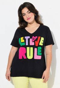Sort bomulds T-shirt med V-hals, der har store, flerfarvede, teksturerede bogstaver, som står "LAD KÆRLIGHEDEN REGERE" i fede, legende skrifttyper.
