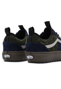 Pár tmavě modrých a olivově zelených tenisek Vans s bílým bočním pruhem, černými patkami a hnědými texturovanými podrážkami na bílém pozadí.