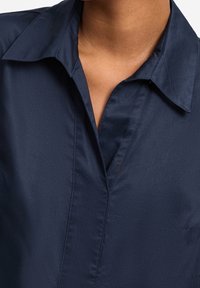 Marineblaue Hemdbluse aus glattem Stoff, mit klassischem Kragen und einer strukturierten Gestaltung mit dezentem Glanz.