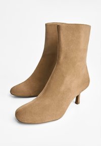 Cizme din piele suede de culoare bej, cu o textură netedă, vârf ascuțit și toc subțire. Design simplu, fără embellishments suplimentare.