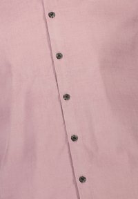 Camicetta rosa chiaro con una texture liscia e una fila di bottoni scuri che scendono lungo il davanti. Il materiale sembra traspirante e morbido.