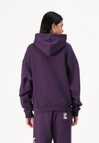 Hanorac oversized mov, cu o glugă mare, manșete cu nervuri și o etichetă cu logo țesut în colțul din dreapta jos. Fabricat dintr-un material moale și confortabil.