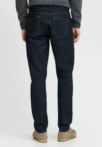 Mørkeblå denimjeans med slim fit, med standard baklommelydesign og subtil søm. Brukt med lysebrune sko.
