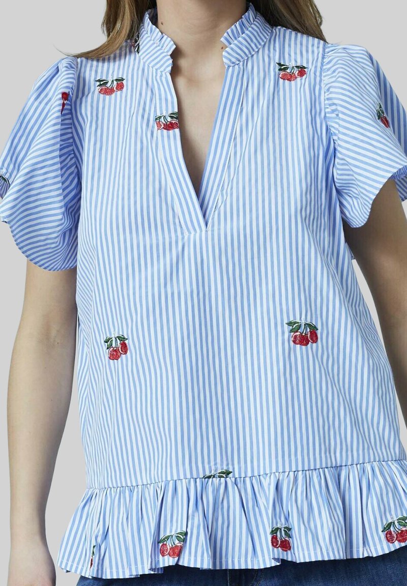 Blå og hvid stribet bluse med flæser i bunden, med kirsebærbroderi på brystet og ærmerne, samt en V-hals design.