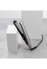 Piastra per capelli con una elegante scocca argentata e piastre in ceramica nera. Presenta pulsanti sul lato e un cavo che si estende dalla base.