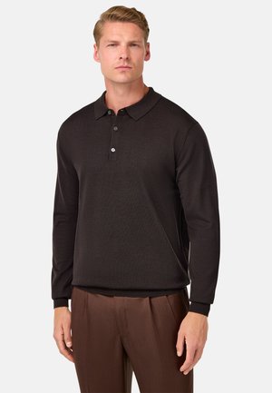 Camisa polo de manga larga negra con una textura suave, que presenta un cuello clásico y una tapeta de tres botones, combinada con pantalones marrones.