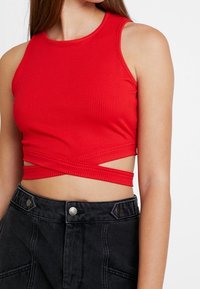 Rode geribbelde crop top met een hoge halslijn en gekruiste bandjes bij de taille, gecombineerd met hoge zwarte denim shorts met accentknopen.
