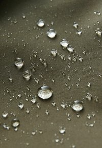 Des gouttes d'eau claires perlent sur une surface en tissu imperméable vert olive texturé, mettant en valeur la résistance à l'eau.
