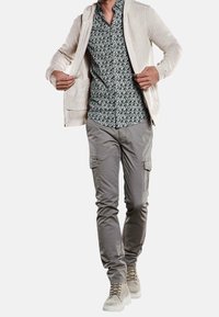 Light beige knit hoodie over a patterned short-sleeve shirt, paired with gray cargo pants and tan boots. The design features a mix of textures.