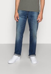 Blå denimjeans med slitningar, rak ben-design, uppvikta fållar, i kombination med vita sneakers. Material: bomullsblandning.