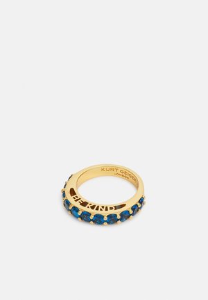 Bague en or avec des pierres bleues autour du bandeau et "BE KIND" découpé à l'intérieur, gravée avec "KURT GEIGER LONDON" sur la face intérieure.
