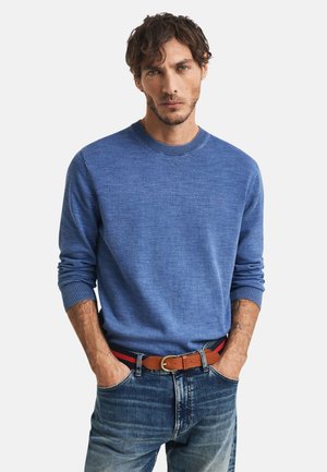 Kék crew neck pulóver puha kötött anyagból, bordás mandzsettákkal, kék farmernadrággal és barna övvel, amely piros és fekete részletekkel rendelkezik.
