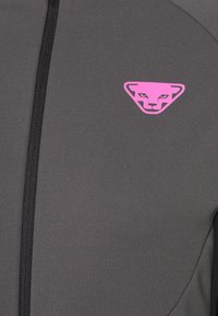 Veste de sport grise avec une texture lisse, dotée d'une fermeture éclair noire et d'un logo triangulaire rose avec un visage de chat stylisé.