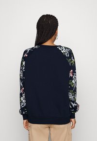 Navy sweatshirt featuring floral patterned sleeves, ribbed cuffs, and hem. Crafted from soft fabric with a relaxed fit.