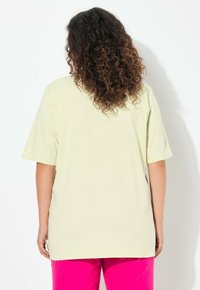T-shirt corto giallo chiaro con una vestibilità rilassata. Tessuto di cotone morbido, texture liscia e orlo dritto. Indossato con pantaloni rosa vivaci.