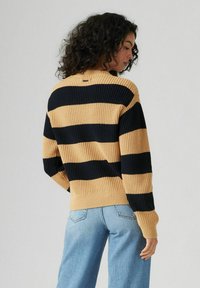 Maglione a righe gialle e nere, texture lavorata a maglia, orlo a coste, con una vestibilità comoda. Abbinato a jeans blu chiaro a vita alta.
