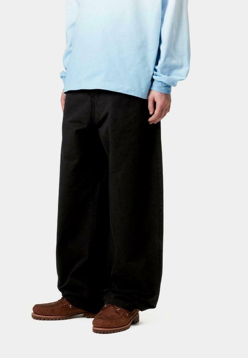 Pantalones anchos negros con una textura suave, combinados con una camisa de manga larga azul clara y zapatos estilo mocasín marrones.