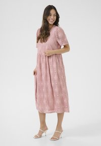Rosa spets midi-klänning med korta ärmar, blommönster, rynkad midja och en flödande siluett. Matchad med vita klacksandaler.