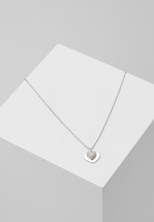 Collier chaîne en argent avec deux pendentifs en forme de cœur, l'un uni et l'autre incrusté de petites pierres claires, présenté sur un cube blanc.