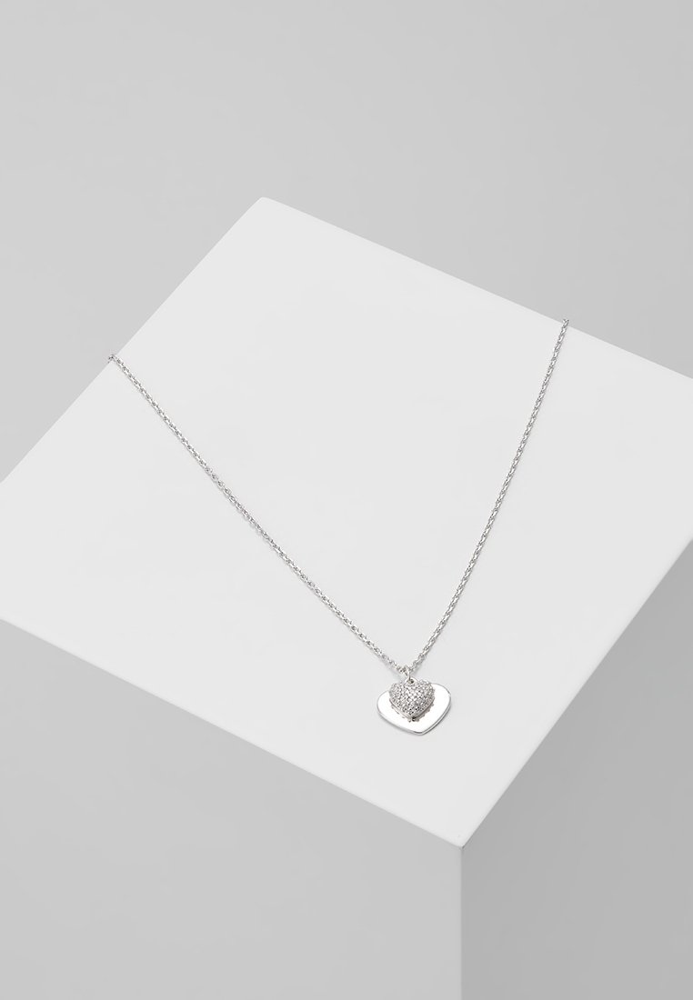 Collier chaîne en argent avec deux pendentifs en forme de cœur, l'un uni et l'autre incrusté de petites pierres claires, présenté sur un cube blanc.