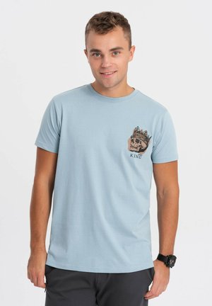 Camiseta de algodón de manga corta en azul claro con un gráfico de una calavera llevando una corona y la palabra "REY" debajo en el lado izquierdo del pecho.