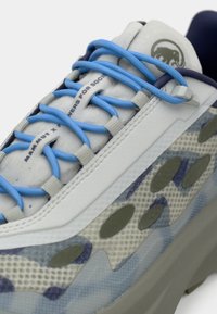 Helle graue Sneaker mit blauen Schnürsenkeln, strukturiertem Mesh-Obermaterial und lila Akzenten. Verfügt über ein auffälliges Logo und eine gepolsterte Sohle.