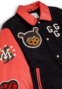 Giacca varsity nera e rossa con maniche in pelle rossa, faccia di orso ricamata, lettere GG e patch a forma di "M" con stelle sulla manica.