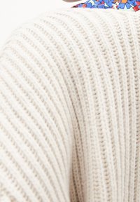 Maglione beige lavorato a maglia con un motivo a coste testurizzato, caratterizzato da un accento floreale colorato sul colletto.
