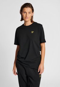 Svart bomullst-shirt med rund halsringning och korta ärmar, med en gul broderad design på vänster bröst.