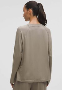 Sweatshirt din țesătură moale, bej deschis, cu un croi lejer, mâneci raglan și guler rotund. Prezintă un detaliu mic cu logo la tiv.