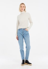 Col roulé beige clair à côtes, coupe décontractée, assorti à un jean taille haute délavé moyen. Bottes de cheville noires à plateforme avec semelles épaisses.