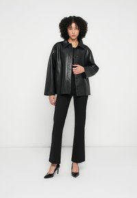 Czarna skórzana kurtka o luźnym kroju, z dużym kołnierzem i guzikami z przodu, zestawiona z czarnymi dopasowanymi spodniami i czarnymi szpilkami.