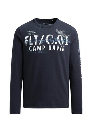 Marineblaue Langarmbluse mit verschiedenen weißen und blauen Aufdrucken, darunter luftfahrtinspirierte Texte und Logos, mit rundem Ausschnitt.