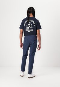 Navy t-shirt with graphic text and image on the back, paired with slim fit, textured navy pants and white sneakers.