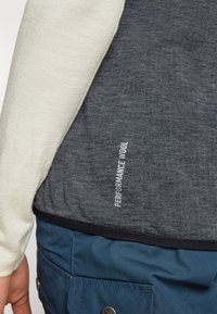 Gray and ivory performance wool top with contrasting textures, featuring side seam branding. The bottom is a dark blue material with a pocket.
