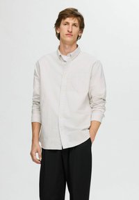 Camicia a righe nei toni chiari, con maniche lunghe e taschino sul petto, abbinata a pantaloni neri. Tessuto dalla texture liscia.