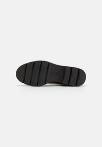 Suela de zapato de goma negra con un diseño texturizado y acanalado que presenta seis secciones prominentes de banda de rodadura, logotipo de marca grabado y detalles de patrón.