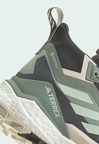 Gestructureerde zwarte en groene sneaker met Gore-Tex-merk. Heeft een geweven mesh bovenwerk, rubberen zool en een uniek schuin ontwerp.