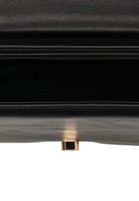 Czarna skórzana torebka z widocznymi złotymi nóżkami u dołu, na białym tle, ukazująca fakturę i detale przeszyć.