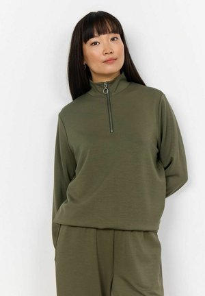 Maslinasto zelena majica sa dugim rukavima i visokim ovratnikom, zatvara se na zip. Ima glatku teksturu i kružni zip dodatak na ovratniku.