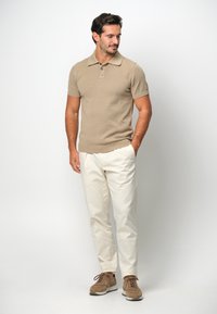 Beige stickad polo med krage och tre knappar, kombinerad med ljuskrämfärgade byxor och bruna mockaskor.