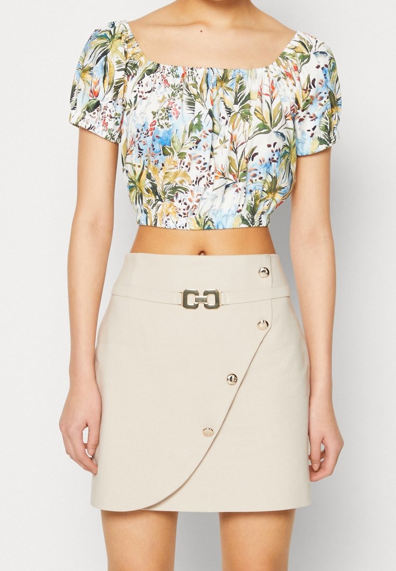 Haut court à fleurs avec manches bouffantes en tissu multicolore, associé à une jupe portefeuille beige avec une boucle dorée et des boutons décoratifs.