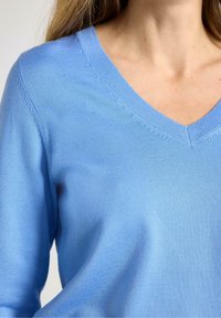 Maglione azzurro chiaro con scollo a V, realizzato in tessuto a maglia fine e liscia. Presenta un collo a coste e una texture morbida. Senza motivi o dettagli visibili.