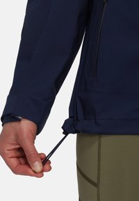 Navy outdoor jacket with a hand adjusting the hem drawstring; features a sleek design and a smooth, water-resistant fabric.