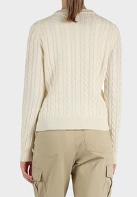 Maglione color crema con motivo a trecce e polsini e orlo a coste, indossato con pantaloni cargo beige, vista posteriore.